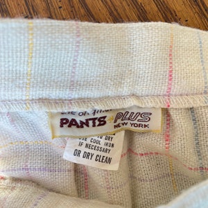 May include: A white, multi-colored plaid fabric with a brown label that reads "Pants Plus New York" and care instructions: "Use to dry, use cool iron if necessary, or dry clean."