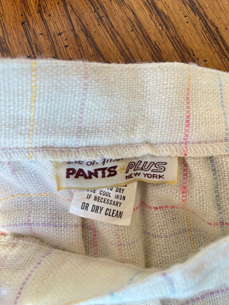 May include: A white, multi-colored plaid fabric with a brown label that reads "Pants Plus New York" and care instructions: "Use to dry, use cool iron if necessary, or dry clean."