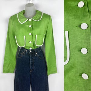 May include: A lime green jacket with white trim on the collar, pockets, and button closures. The long-sleeved jacket is paired with dark blue denim jeans. The jacket has a round collar and two front pockets.
