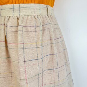 May include: A beige skirt with a multi-colored plaid pattern. The skirt has a waistband with a button closure.