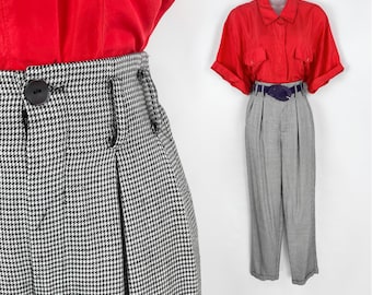 May include: Black and white houndstooth high-waisted pants with pleats and a button closure. The pants are paired with a red short-sleeved button-down shirt and a purple belt.