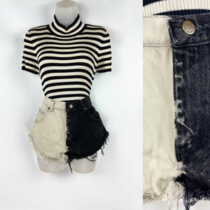May include: A black and white striped short-sleeve turtleneck shirt paired with two-tone denim shorts. The shorts are half light beige and half black, with frayed edges. The outfit is displayed on a mannequin.