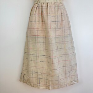 May include: A beige midi skirt with a plaid pattern in shades of blue, red, and yellow. The skirt has a high waist and a straight silhouette.