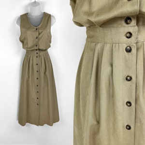 May include: A tan sleeveless dress with a button-down front. The dress features a fitted bodice and a pleated skirt that falls to the mid-calf. The dress is displayed on a mannequin against a white background.