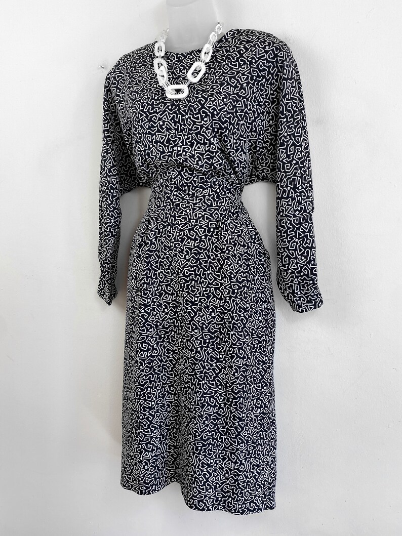 Puede incluir: Un vestido de estampado geom&eacute;trico en blanco y negro con mangas largas. El vestido tiene un corpi&ntilde;o ajustado y una falda ligeramente acampanada. El vestido est&aacute; en un maniqu&iacute; blanco.