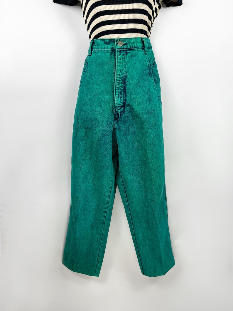 May include: Bright green acid wash jeans with a high waist. The jeans have a classic five-pocket design and a button and zipper closure. The pants are shown with a black and white striped top.
