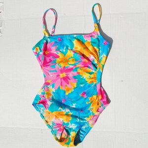 K&ouml;nnte beinhalten: Ein einteiliger Badeanzug mit floralem Muster in Blau, Rosa und Gelb mit d&uuml;nnen Tr&auml;gern.