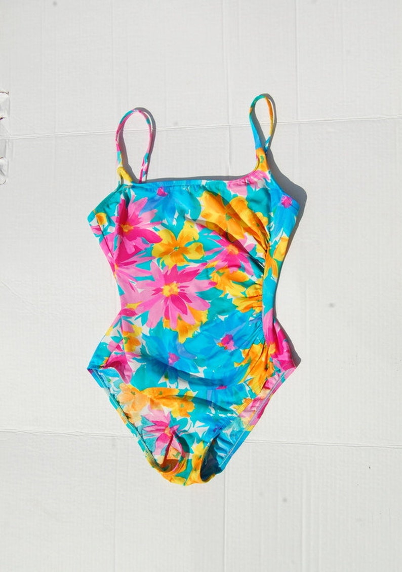 K&ouml;nnte beinhalten: Ein einteiliger Badeanzug mit floralem Muster in Blau, Rosa und Gelb mit d&uuml;nnen Tr&auml;gern.