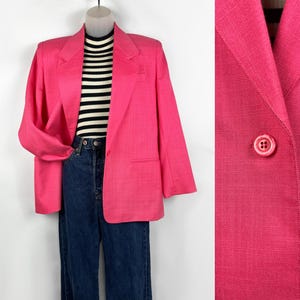 May include: A bright pink blazer with a classic design, featuring a two-button closure and a tailored fit. The blazer is paired with a black and white striped top and blue jeans. The blazer is a vibrant addition to any wardrobe.
