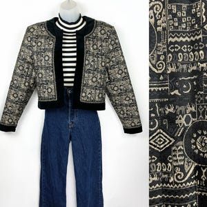 May include: A black and gold cropped jacket with a velvet trim and a geometric pattern. The jacket is worn over a striped shirt and blue jeans.
