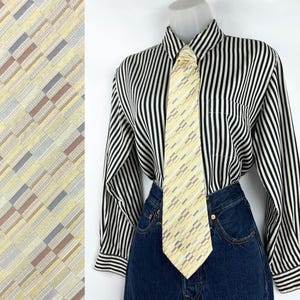 May include: A yellow tie with a geometric pattern of rectangles in gray, brown, and blue is displayed. The tie is paired with a black and white striped button-down shirt and dark blue denim jeans. The tie's design is also shown in a close-up view.