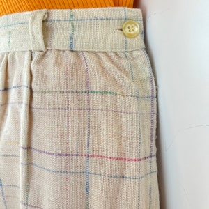 May include: Beige plaid pants with a button closure. The pants are made of a woven fabric with a subtle texture.