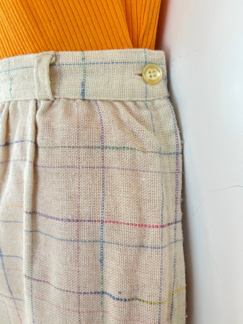 May include: Beige plaid pants with a button closure. The pants are made of a woven fabric with a subtle texture.