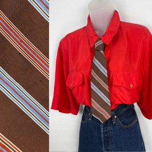 May include: A red short-sleeved button-down shirt with a brown and blue striped tie. The shirt has two large pockets on the front.