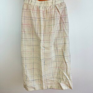 May include: A beige skirt with a multi-colored plaid pattern. The skirt has a waistband and a straight silhouette.
