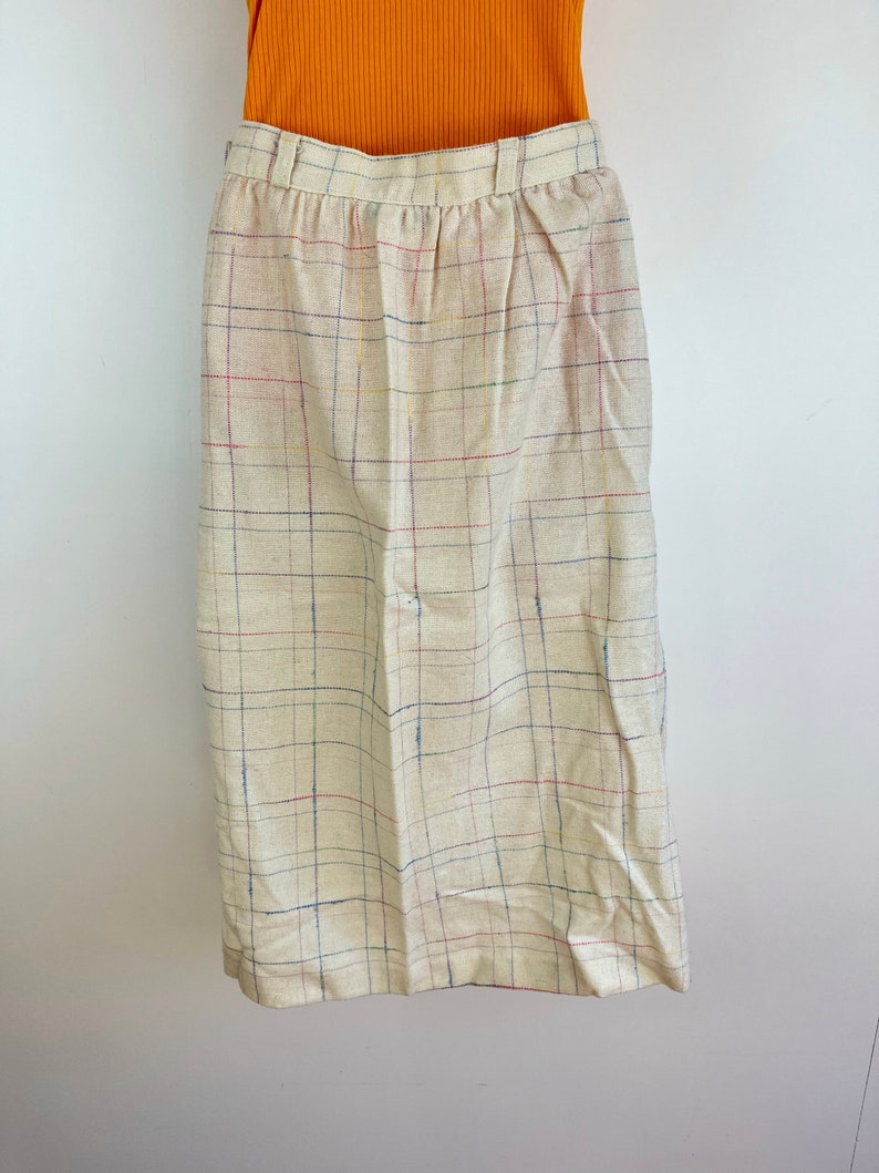 May include: A beige skirt with a multi-colored plaid pattern. The skirt has a waistband and a straight silhouette.