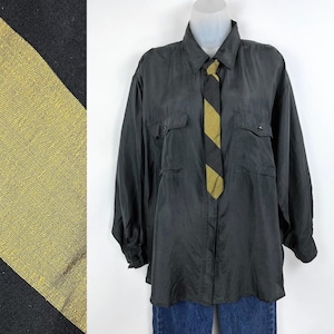 May include: A black silk shirt with a long sleeve and two flap pockets. The shirt has a black and gold striped tie.