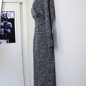 Puede incluir: Un vestido estampado en blanco y negro con escote en V y mangas 3/4. El vestido est&aacute; colgado en una pared blanca.