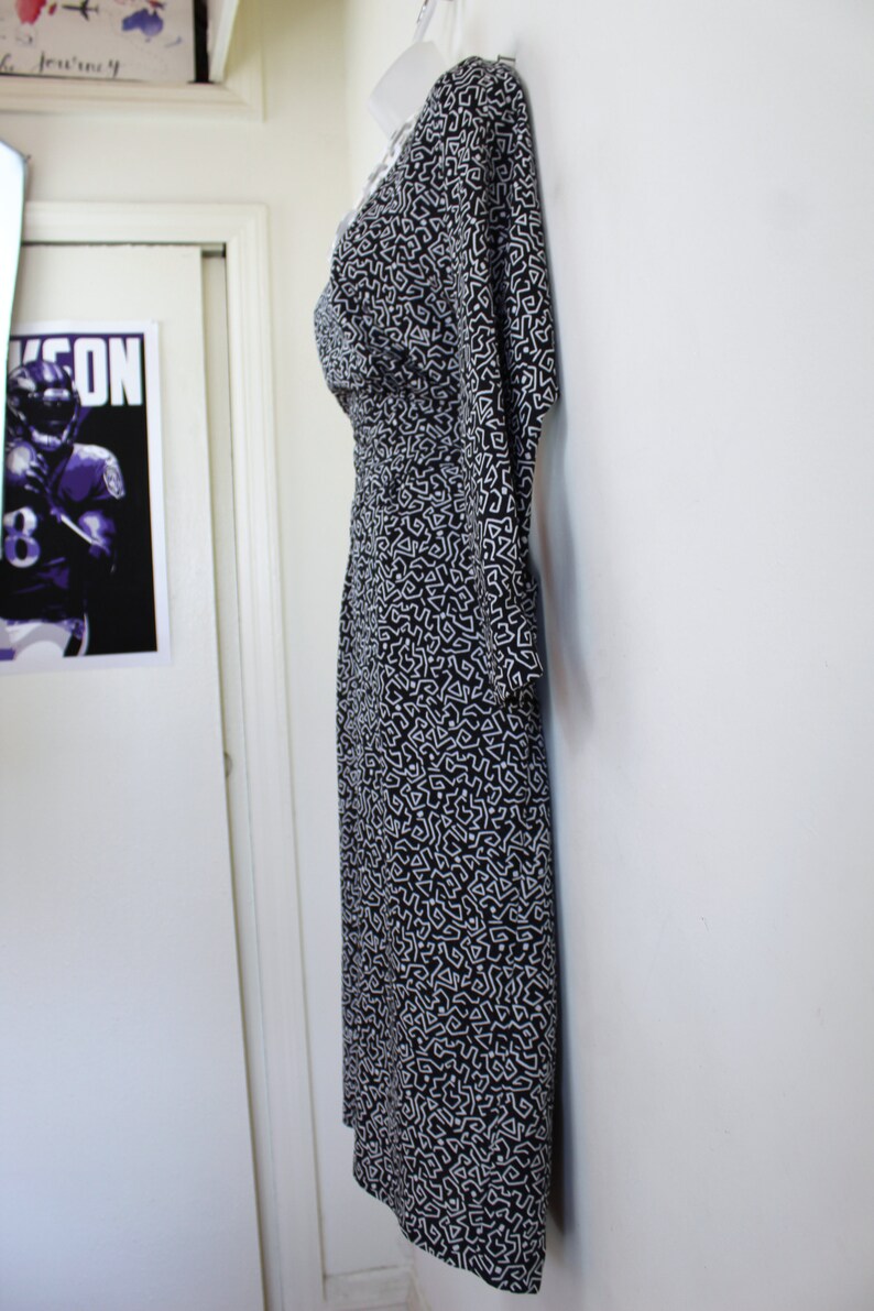 Puede incluir: Un vestido estampado en blanco y negro con escote en V y mangas 3/4. El vestido est&aacute; colgado en una pared blanca.