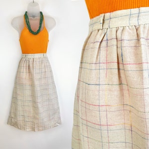 May include: A beige midi skirt with a plaid pattern in shades of blue, red, and yellow. The skirt has a high waist and a gathered waistband.