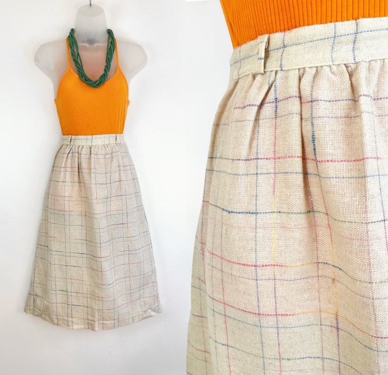 May include: A beige midi skirt with a plaid pattern in shades of blue, red, and yellow. The skirt has a high waist and a gathered waistband.