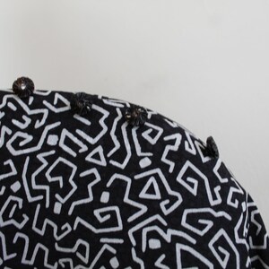 Puede incluir: Tela negra y blanca con un patr&oacute;n geom&eacute;trico. La tela tiene una superficie texturizada y est&aacute; decorada con peque&ntilde;os botones negros.