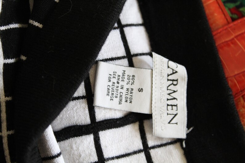 May include: A white tag with black text attached to a black and white checkered fabric. The tag reads "CARMEN", "S", "80% RAYON 20% NYLON", "MADE IN CHINA", "RN# 93178", "SEE REVERSE FOR CARE".