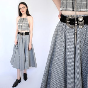 May include: A black and white gingham midi skirt with a wide black belt and a large silver buckle. The skirt is full and flowing, and the belt has a silver chain attached to it.