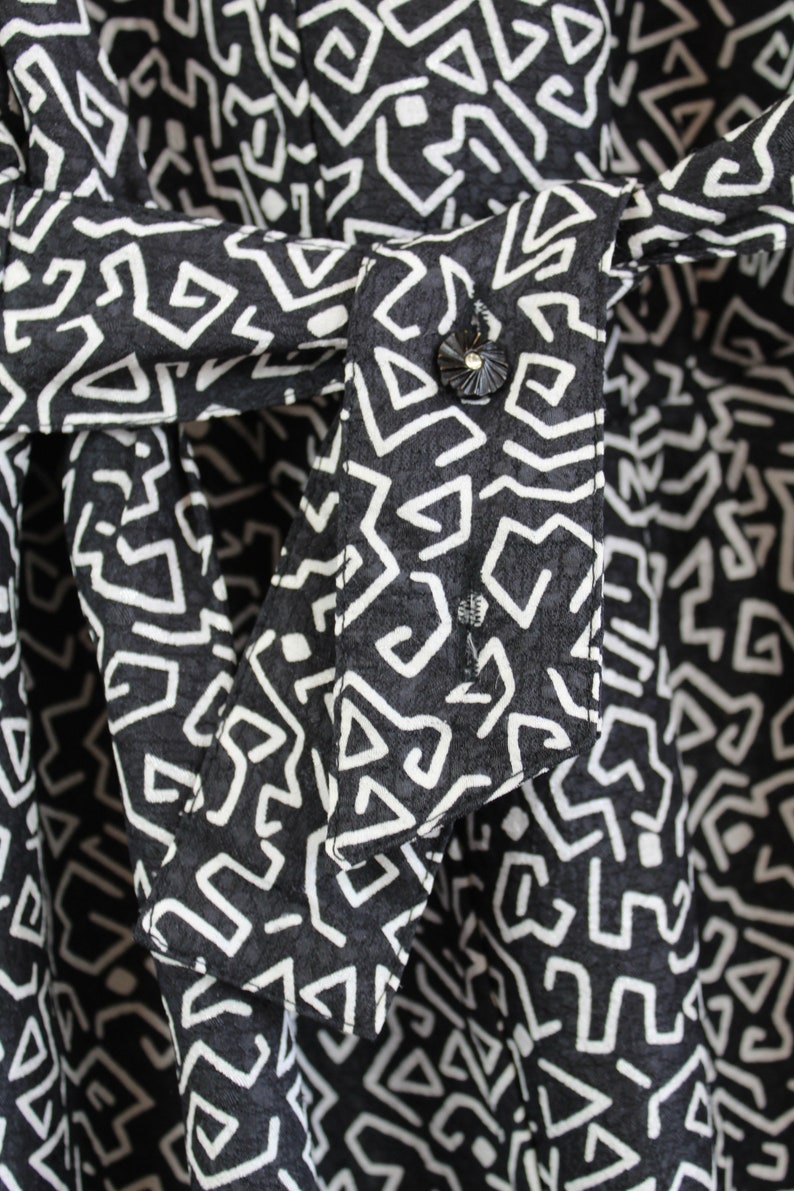 Puede incluir: Primer plano de una tela con estampado blanco y negro con un bot&oacute;n blanco. La tela tiene un dise&ntilde;o geom&eacute;trico con una superficie texturizada.