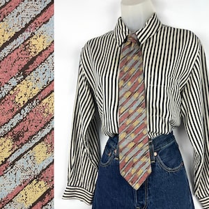May include: A patterned tie with diagonal stripes in shades of red, yellow, gray, and blue. The tie is paired with a black and white striped button-down shirt and blue denim jeans.