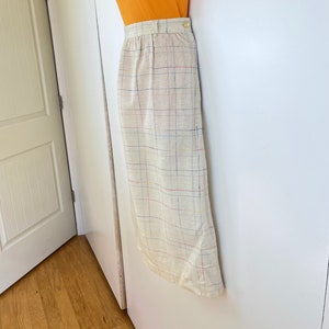 May include: A beige skirt with a multi-colored plaid pattern. The skirt has a high waist and a straight silhouette.
