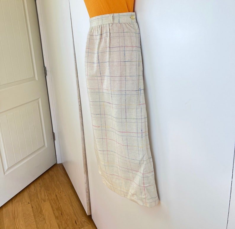 May include: A beige skirt with a multi-colored plaid pattern. The skirt has a high waist and a straight silhouette.