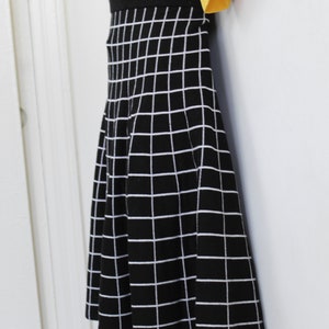 May include: A black and white checkered skirt with a flared silhouette. The skirt is made of a knit fabric and has a black waistband.