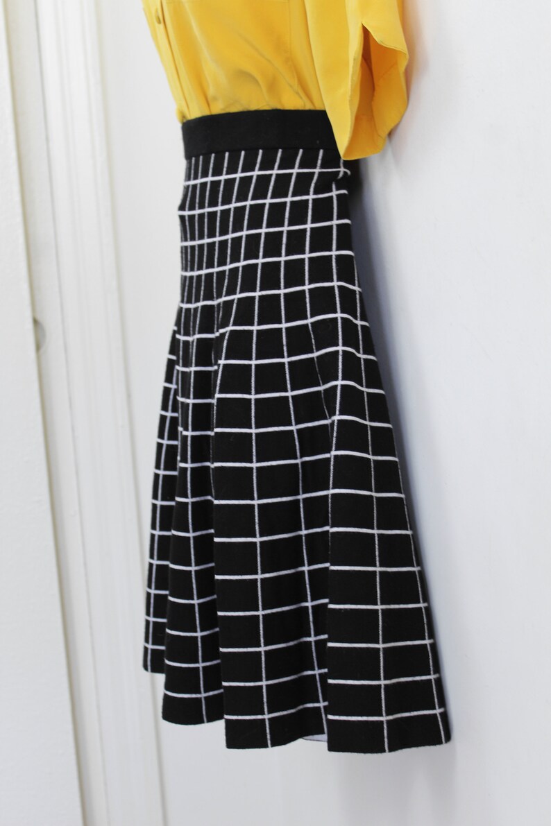 May include: A black and white checkered skirt with a flared silhouette. The skirt is made of a knit fabric and has a black waistband.