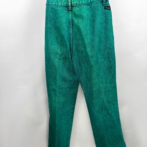 May include: Bright green acid wash jeans with a black Wrangler label on the back pocket. The jeans are paired with a black and white striped top. The pants have a classic five-pocket design and a straight leg.