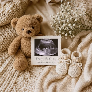Könnte beinhalten: Ein brauner Teddybär, ein Ultraschallbild und gestrickte Babyschuhe auf einer beigen Decke. Das Ultraschallbild zeigt "Baby Anderson, Due December 2025". Weiße Blumen im Hintergrund. Eine Babyankündigung.