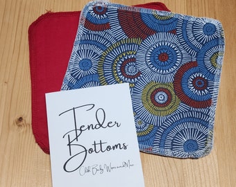 Puede incluir: Dos toallitas para bebé de tela, una roja y otra con un patrón geométrico azul, amarillo y rojo. Las toallitas están dobladas y apiladas una encima de la otra. Una tarjeta blanca con el texto "Tender Bottoms Cloth Baby Wipes and More" está delante de las toallitas.