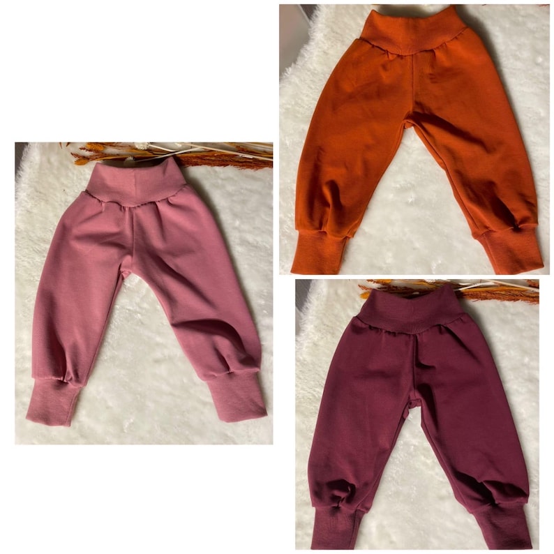 Puede incluir: Tres pantalones de beb&eacute; en diferentes colores: rosa empolvado, naranja quemado y burdeos. Los pantalones tienen una cintura alta y pu&ntilde;os en los tobillos. La tela parece ser un material de punto suave, adecuado para la comodidad y la flexibilidad.