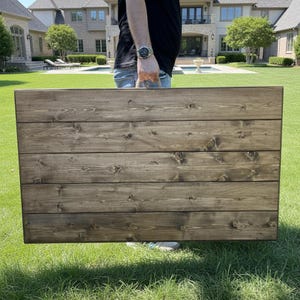 Puede incluir: Un letrero de madera rectangular grande con una mancha marr&oacute;n oscuro. El letrero est&aacute; construido con tablones de madera horizontales, con nudos y vetas visibles. El letrero se sostiene al aire libre sobre un c&eacute;sped.