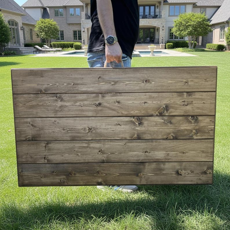 Puede incluir: Un letrero de madera rectangular grande con una mancha marr&oacute;n oscuro. El letrero est&aacute; construido con tablones de madera horizontales, con nudos y vetas visibles. El letrero se sostiene al aire libre sobre un c&eacute;sped.