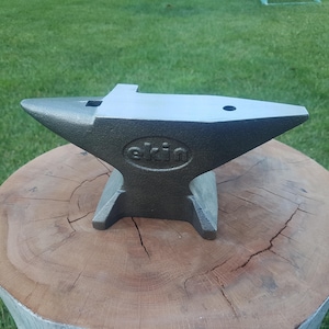 Puede incluir: Un yunque de metal gris con la palabra "ekin" grabada en relieve en el lateral. El yunque está sobre un tronco de árbol.