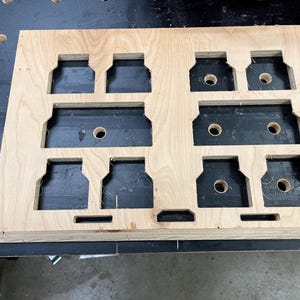 May include: A wooden board with multiple cutouts, each with a circular hole in the center. The board is light brown and has a smooth finish.