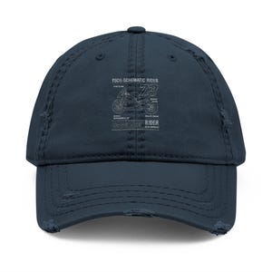 Puede incluir: Gorra de béisbol azul marino desgastada con un esquema de motocicleta y el texto "TECH-SCHEMATIC RIDER". La gorra tiene una visera curva y un aspecto desgastado, con detalles envejecidos en los bordes.