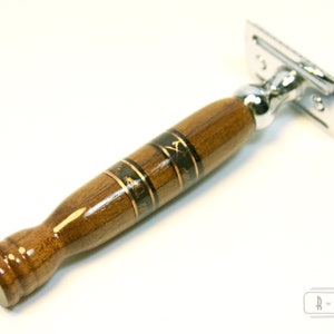 Puede incluir: Una navaja de afeitar de seguridad con mango de madera. El mango es marr&oacute;n con detalles dorados y negros. El mango tiene un dise&ntilde;o decorativo.