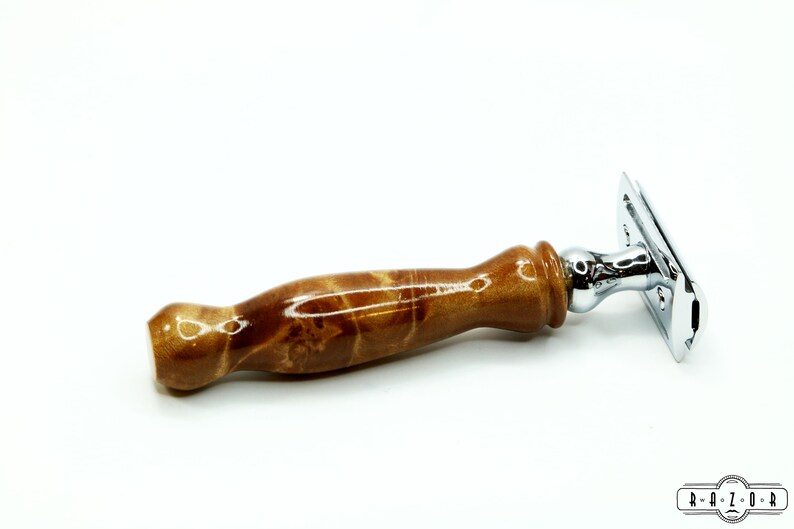 K&ouml;nnte beinhalten: Ein Sicherheitsrasierer mit einem Holzgriff und einem verchromten Kopf. Der Griff ist hellbraun mit einem marmorierten Muster.