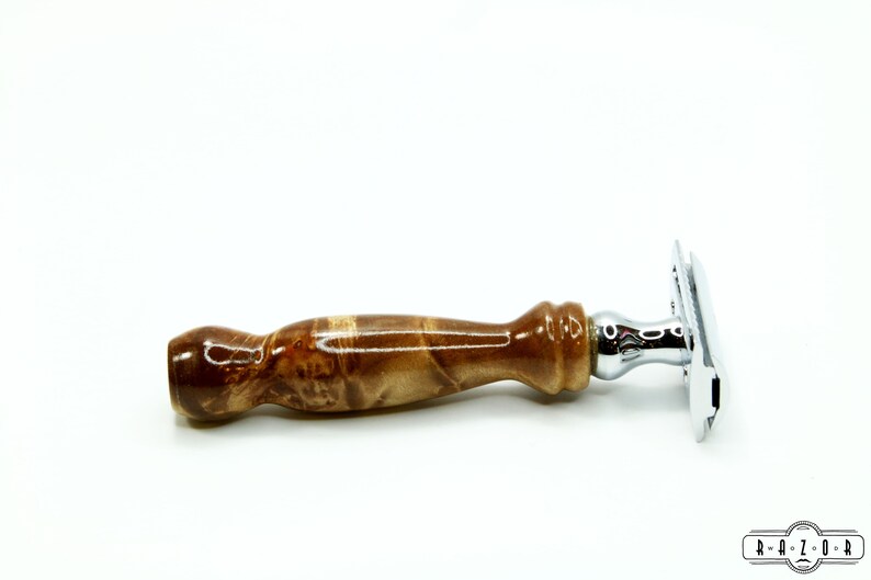 K&ouml;nnte beinhalten: Ein Sicherheitsrasierer mit einem verchromten Kopf und einem braunen Holzgriff. Der Griff hat ein marmoriertes Muster.