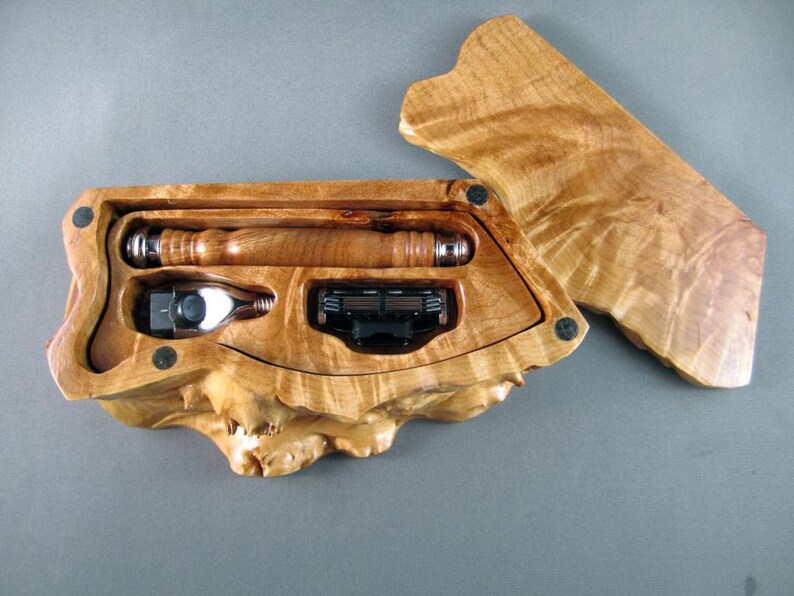 Op de afbeelding: Een houten doos met een burl-houten afwerking, open om een scheerkwast, scheermes en een set bladen te onthullen. De doos is gemaakt van natuurlijk hout en heeft een unieke, organische vorm.