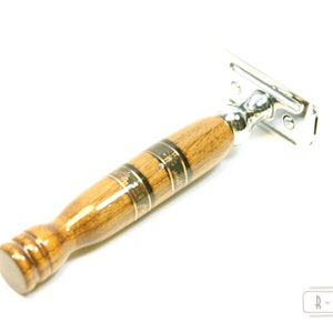 Puede incluir: Una navaja de afeitar de seguridad de madera con una cabeza cromada y un mango de madera marr&oacute;n con detalles dorados. El mango tiene un patr&oacute;n decorativo.