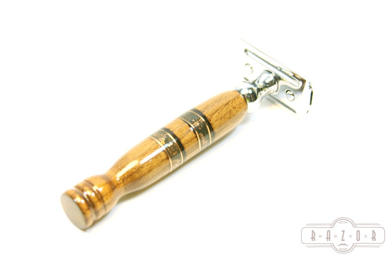 Puede incluir: Una navaja de afeitar de seguridad de madera con una cabeza cromada y un mango de madera marr&oacute;n con detalles dorados. El mango tiene un patr&oacute;n decorativo.