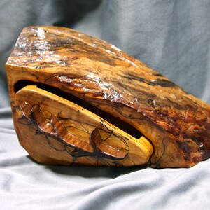 May include: A wooden box with a natural wood finish and a unique, irregular shape. The box has a hinged lid and a drawer that slides out. The wood has a beautiful grain pattern and is polished to a high sheen.